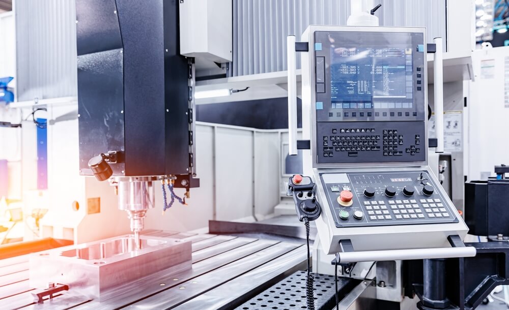 CNC frezarka z panelem sterowania i monitorem nad metalowym detalem na stole roboczym